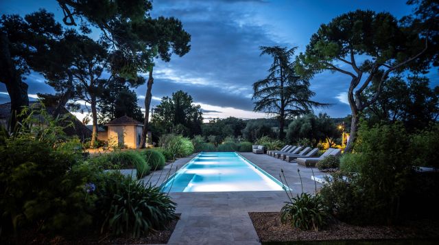 Piscine extérieure vue de nuit éclairée avec couché de soleil sur le jardin méditerranéen de la Villa Roubia